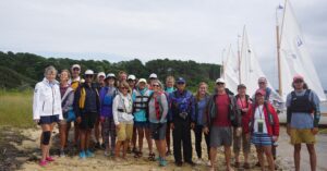 A group photo of sailors on Sipson Island, with their catboats beached behind them.